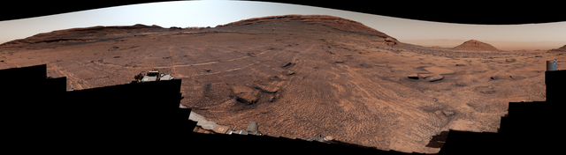 A panoramic view of a sweeping Martian plain covered in patterned fractures leading toward distant hills showcases the terrain explored by NASA's Curiosity rover to investigate the planet's past environment.