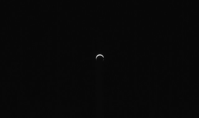 Against a vast black background, a small white crescent shape occupies the center of the image. The crescent is thickest at top and open on the bottom.