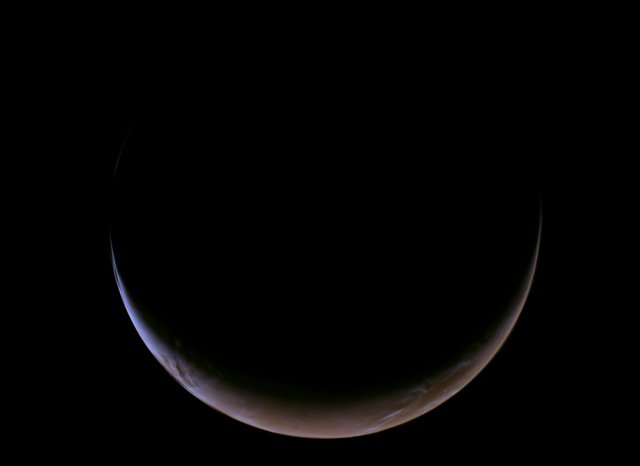 A slender, glowing crescent of Mars curves across the bottom of a completely black void, revealing its dusty reddish-orange surface and a thin, hazy blue atmospheric glow along the illuminated edge.