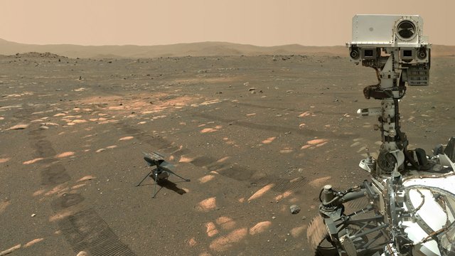 On the right hand side of the image, the Perseverance Mars rover looks forward toward the camera. In the lower left, the Ingenuity helicopter sits on the surface of Mars.