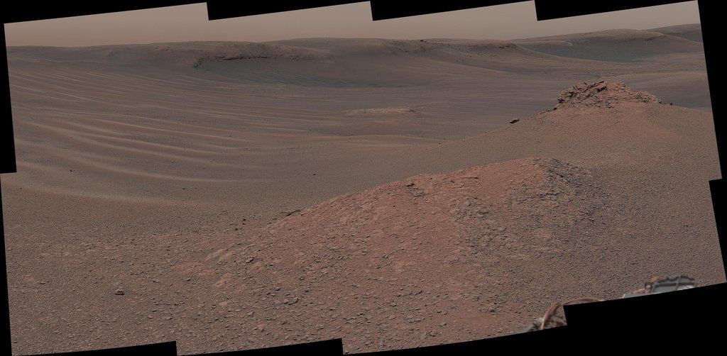 A downward view shows the Curiosity rover’s robotic arm over a flat, cracked, brown Martian rock. Yellow arrows and text indicate three distinct circular holes in the rock — “Groken,” “Mary Anning,” and “Mary Anning 3” — made by the rover’s drill.