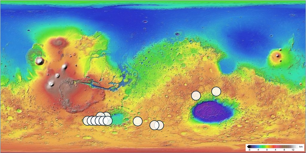 A colorful topographic map of Mars displaying planetary elevations from low blue basins to high red volcanic plateaus, marked with white circular dots across the southern hemisphere.