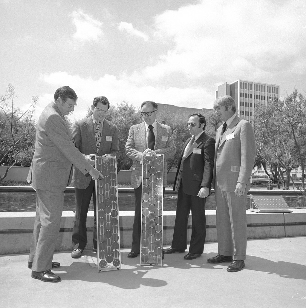 Five men in suits holding two photovoltaic solar panels