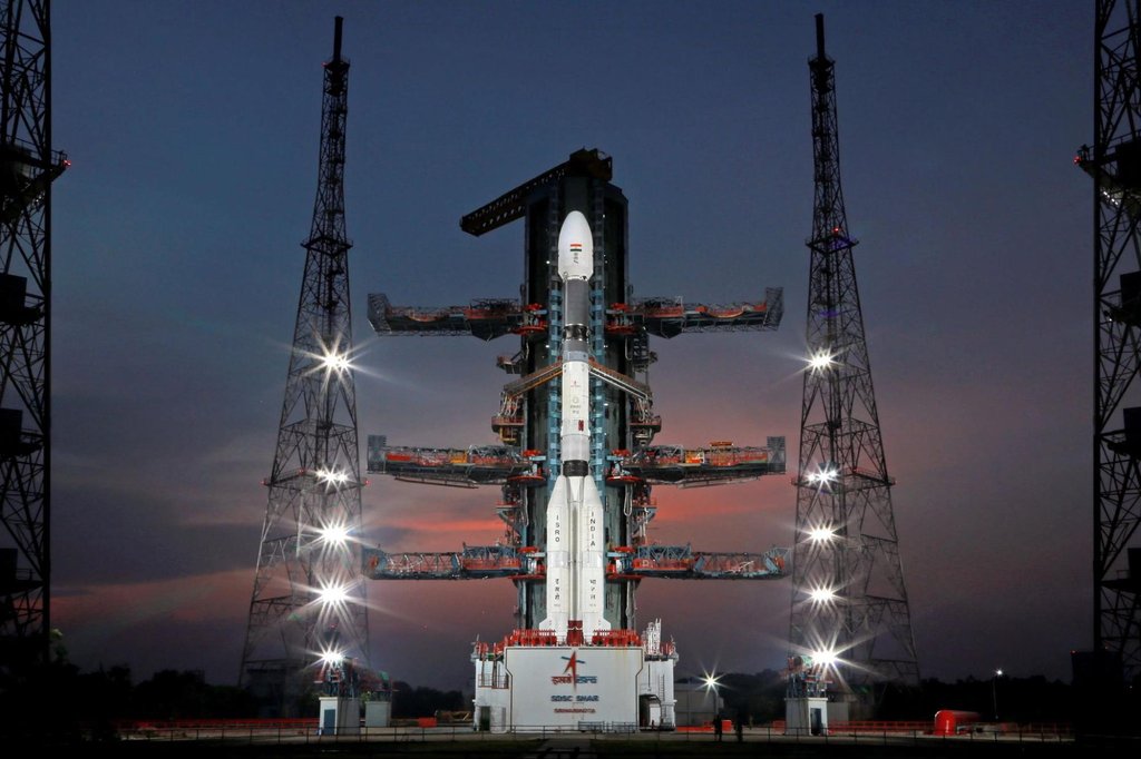 Rocket on launch pad in India, lit by flood lights on surrounding towers.
