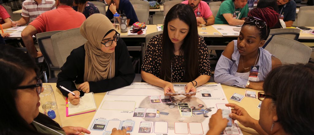 A group of educators sits around a table with a printed out board game and cards.